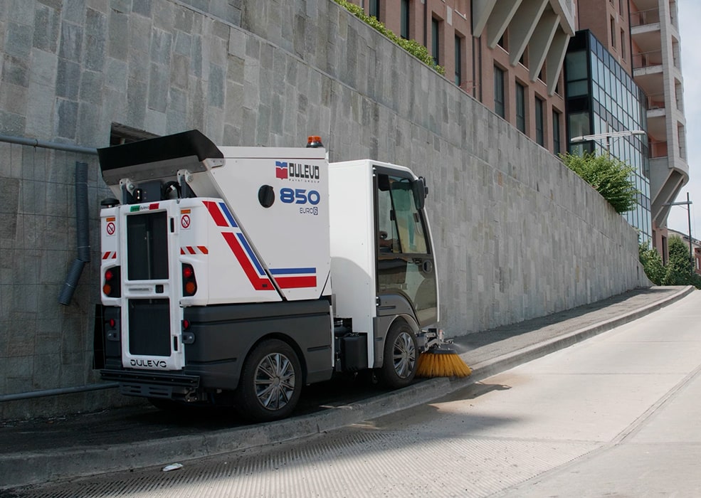 A Dulevo 850 Sweeper cleaning a sidewalk along a road.