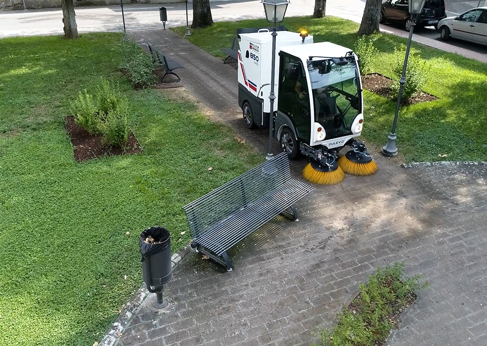 A Dulevo 850 Sweeper cleaning a brick pedestrian path in a small park.