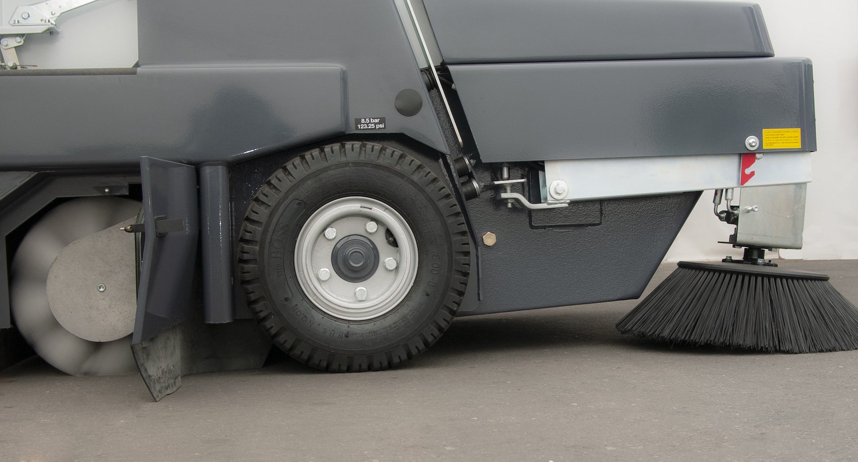 A side view of the bottom half of a Dulevo 120 sweeper, showing its main broom, non-marking tire, and side brush.